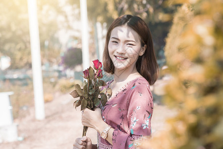手持红玫瑰在公园里微笑的亚洲女吸引人的孩天图片