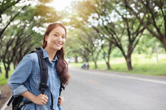 航程冒险亚裔女游客和随身行李等候汽车的亚洲妇女以及自由旅行者站在路边举起手来的妇女搭便车图片