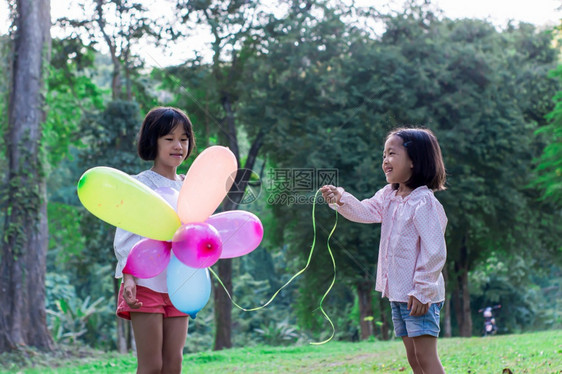 自由积极的两名女孩在公园户外的内持有多彩玩具气球保持图片