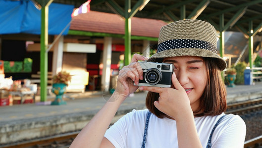 复古相机美丽年轻漂亮的亚洲女旅行者身穿随意风格戴帽子拍照在火车站的铁路平台上用旧相机照片旅行中的生活方式概念白色的摄影师背景