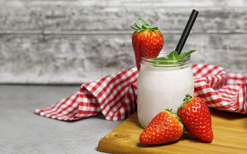 在一个玻璃罐子里的草莓新鲜凉冰滑奶昔有饮用稻草薄粉叶和灰色本底成熟的草莓以及一个带复制空间的木剪板春天粉色的抗氧化剂图片