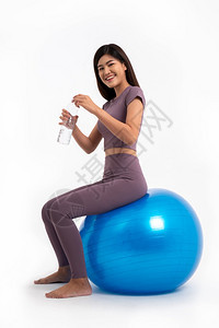 努力女孩健康的亚洲妇女坐在与世隔绝的白背景健身球上喝清洁水良好健康的概念从锻炼开始健身房图片