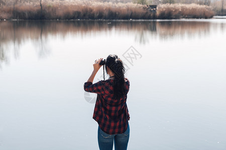 探索穿着双目望远镜和格子衬衣的湖角码头上黑发年轻女人享受背包客图片