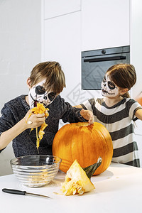 季节家孩子们两个有头骨脸涂颜料的小孩在厨房里切南瓜图片