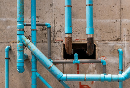 水泥墙上混凝土蓝水塑料管道在公寓楼的水泥墙上建有蓝色塑料管的在建筑物的卫生设备系统中安装一个有混凝土天花板式纹理抽象背景的自来水图片