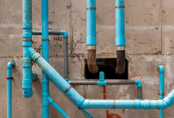水泥墙上混凝土蓝水塑料管道在公寓楼的水泥墙上建有蓝色塑料管的在建筑物的卫生设备系统中安装一个有混凝土天花板式纹理抽象背景的自来水图片