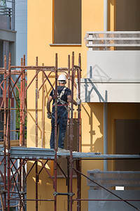 白色的为了戴蓝安全帽的工人在建筑地的脚手架上作一名建筑人在地的脚手架上作男人图片