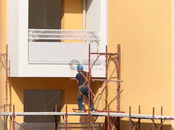 工程师一种男人戴蓝色安全帽的工人在建筑地的脚手架上作一名建筑人在地的脚手架上作图片