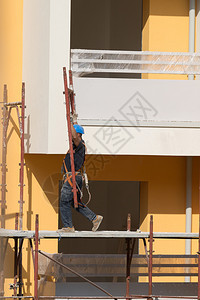 男人行业专的戴蓝色安全帽工人在建筑地的脚手架上作一名建筑人在地的脚手架上作图片
