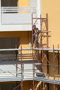建筑学领班职业戴蓝色安全帽的工人在建筑地的脚手架上作一名建筑人在地的脚手架上作图片