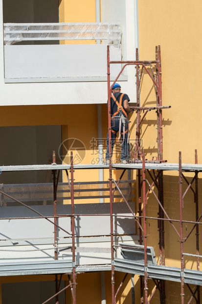 建筑学领班职业戴蓝色安全帽的工人在建筑地的脚手架上作一名建筑人在地的脚手架上作图片