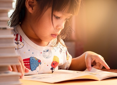 一个可爱的小女孩在读一本书坐家里桌子上呆着隔离冠状流行在家上学的概念快乐桩积极图片