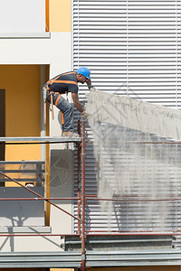 工程师头盔BlueHardhat在建造大楼筑工地一个脚手架上工作与BlueHardhat一起工作人图片