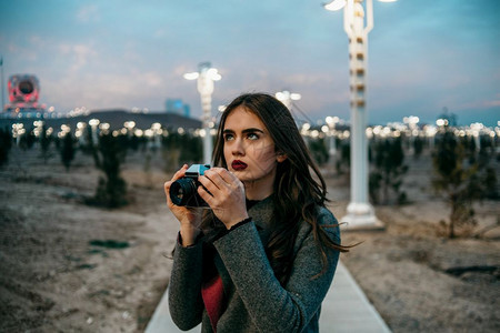 女士晚上在勃伦迪丝袜和灰色大衣的年轻美少女日落时用古董摄影机畅快图片