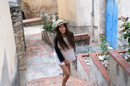 相机城市千禧一代年轻快乐的少女穿着暑期服装和帽子站在楼梯室外看摄影机时站立在楼梯上图片