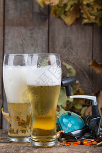 人造的以渔具和玻璃为背景用橡树叶在旧木板上装着啤酒准备铸件图片