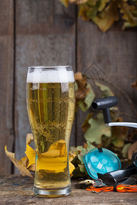 喝摇晃的木头以渔具和玻璃为背景用橡树叶在旧木板上装着啤酒图片