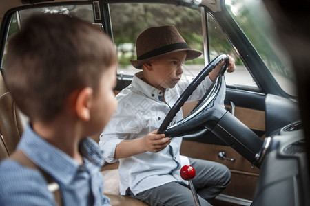 快乐的孩子一种两个穿古老衣服的白人小男孩坐在一辆旧车里图片
