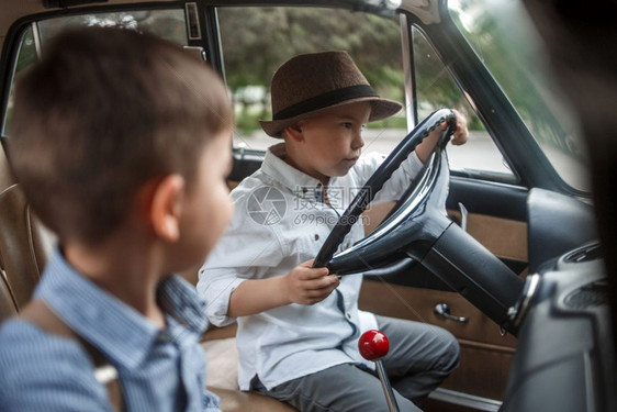 快乐的孩子一种两个穿古老衣服的白人小男孩坐在一辆旧车里图片