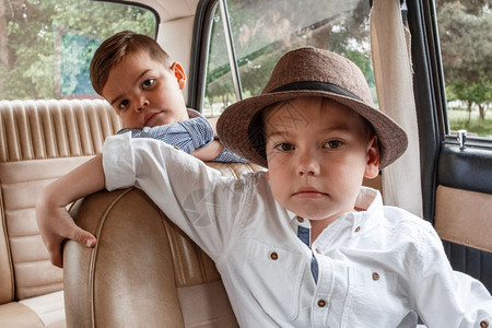 人们快乐的两个穿古老衣服的白人小男孩坐在一辆旧车里汽图片