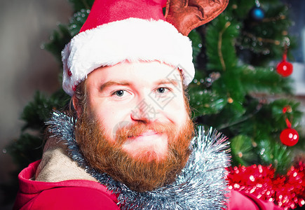 穿着圣诞老人红色西装的长胡子男肖像在圣诞树背景下看着摄影机选择焦点在圣诞老人红衣服中留胡子男选择重点在圣诞老人红衣服中留胡子人相图片