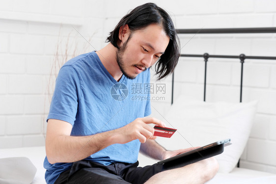 开支持有信用卡并使数字平板电脑在家中线购物商业和技术概念数字营销随意生活方式的年轻亚洲男子持信用卡和使数字片件在家网上购物数字营图片