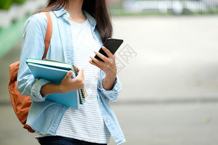 拿着书背着包的女学生在使用智能手机图片