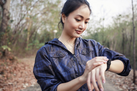 亚洲女跑者检查智能手表健身追踪器在慢跑和步腿后微笑活动运服图片