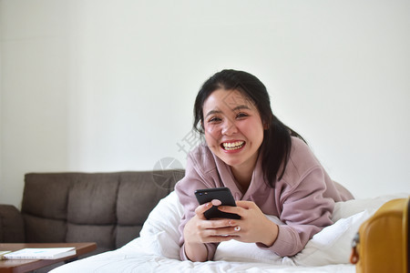 无线的使用移动智能手机的妇女是离子卧室白色的坐着图片