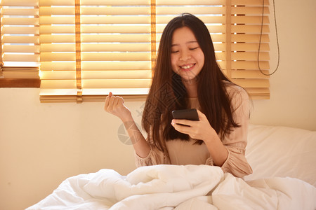 人们使用移动智能手机的妇女是离子卧室保持快乐的图片