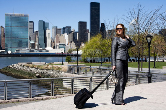 外部灰色的身着西装和墨镜背行李钱包站在纽约市天线和联合国大楼前的一个公园纽约中白衣和墨镜拉丁美洲女企业家创者她们站立在天窗和联合图片