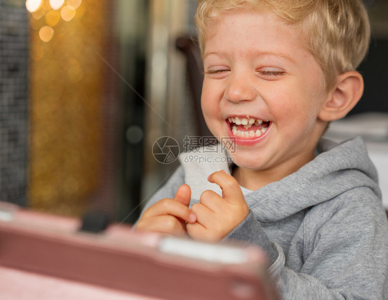 坐在高椅子上的婴儿男孩在餐厅玩耍微笑着快乐的容在光背景下有着漂亮的波克横向相片眼睛水平的散景图片