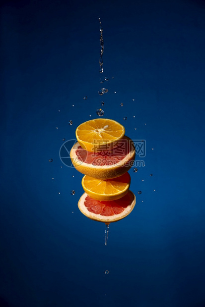 自然漂浮的橙色和葡萄果片在蓝色纹质底上与水滴一起飘浮营养图片