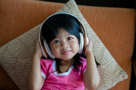 闲暇放松快乐的亚洲女孩微笑并享受在沙发客厅用耳机收听音乐无线的图片