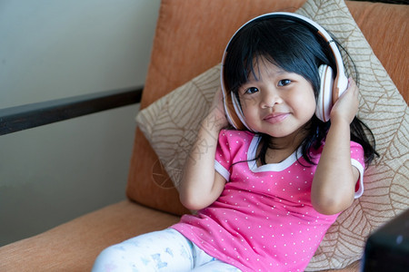 技术手机无线的快乐亚洲女孩微笑并享受在沙发客厅用耳机收听音乐图片