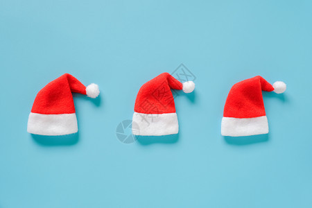 服装三件红色圣诞老人礼帽蓝色背景的红脸卡片布局顶端视图平板模用于设计卡片请帖冬季假日构成三个红色圣诞老人礼帽子蓝色背景的红纸牌布图片