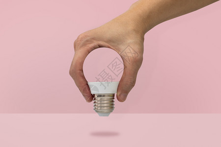 简单的明亮白色手握着在粉红背景上隔离的灯泡形状最小想法概念图片