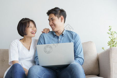 长椅妻子坐在沙地上的亚洲情侣坐在沙发上使用笔记本电脑在室内图片