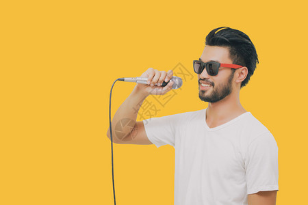 演员乐趣音带着胡子的亚洲英俊男笑着歌唱在黄色背景下被孤立的麦克风图片