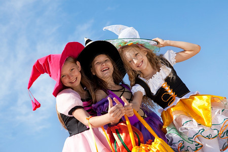 摄影人们巫婆三个美丽的微笑小女孩在彩色巫服装中举起缩拇指看着镜头带诡计或装袋图片