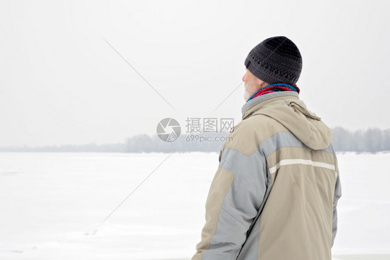 观看薄片一个穿着羊毛帽防水外套和羊毛帽的男人在一个寒冷而悲伤的冬天清晨在雪下看着Dnieper河宁静图片