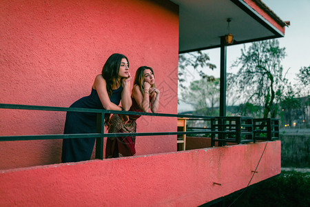 两个年轻的天主教女青年在阳台上观看日落的光芒放松他们友谊图片