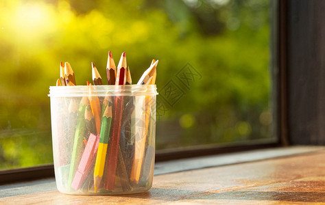 变化彩色铅笔放在一个塑料圆箱里放在窗边的木制桌子上阳光照耀的灯下五彩缤纷锋利的图片