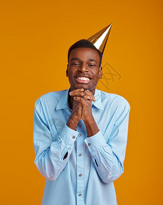 欢快的男人在帽子上黄色背景的笑脸男子得到一个惊喜事件或生日庆典等待一个喜快乐男人在帽子上生日庆典微笑吸引人的为了图片