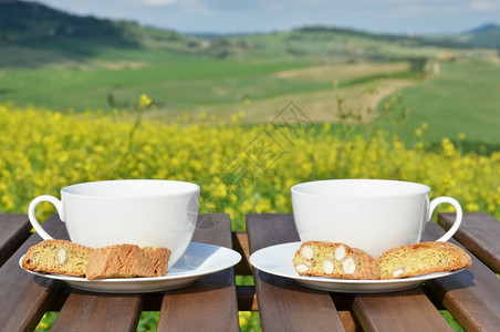 意大利语饼干比斯科蒂木制桌上的两个咖啡杯和罐子意大利托斯卡纳风景图片