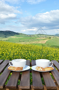 春天木制桌上的两个咖啡杯和罐子意大利托斯卡纳风景饼干方格的图片