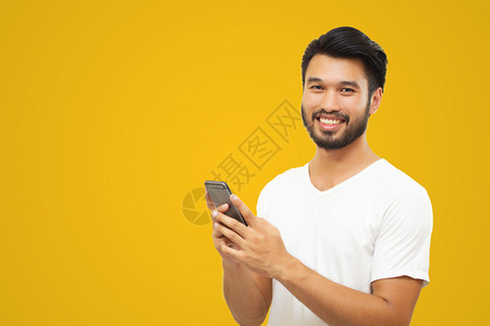 亚洲商人英俊帅哥长胡子微笑在黄色背景下使用智能手机黄色的时尚快乐图片