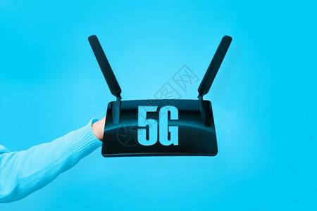 技术手持黑色wifi路由器和蓝色背景上5G的刻字沟通天线图片