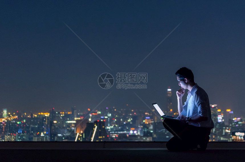 疲劳的使用膝上型计算机在夜间观看城市商业成功和技术概念的风景下深夜工作利用笔记本电脑对城市商业成功和技术概念进行夜间观察时建造图片