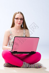 一个年轻美丽的女孩使用她笔记本电脑她看着工作室垂直的青少年图片